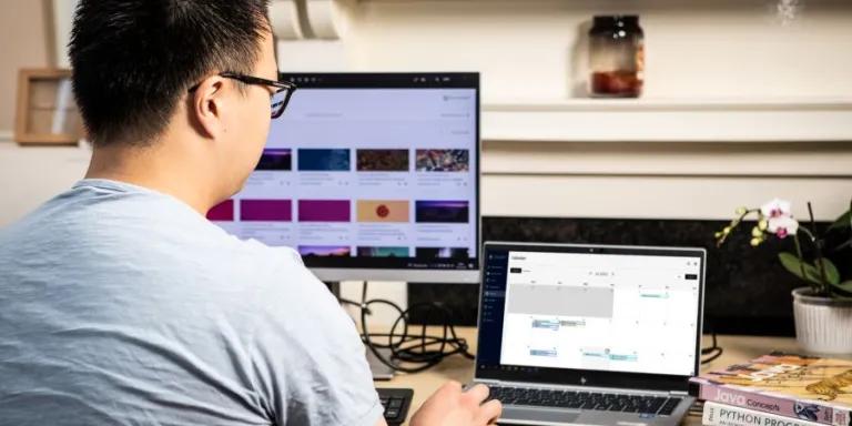 student sat at desk looking at computer screen and laptop