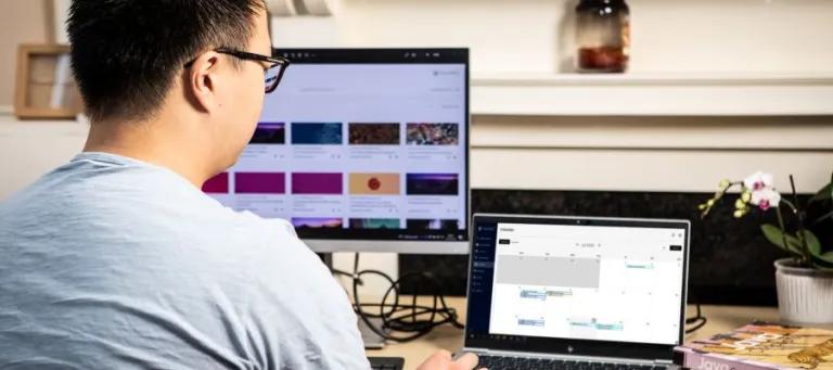 student sat at desk looking at computer screen and laptop